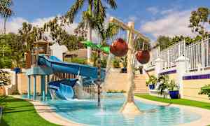 En vandlegeplads med en blå rutsjebane og vandstråler samt dekorative palmer. (AI-genereret tekst)