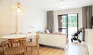 En lys og moderne indrettet stue med et spisebord, en sofa og en klapvogn ved glasdøren. (AI-genereret tekst)