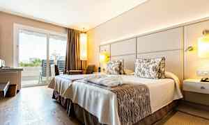 Hotelværelse med to senge og indretning i neutrale toner. Udsigt til balkon gennem glasdøre. (AI-genereret tekst)