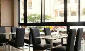 En restaurant med borde og stole, med udsigt til en gårdsplads gennem en stor glasrude. (AI-genereret tekst)