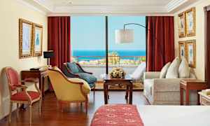 Værelse med røde gardiner, møbler og udsigt over havet. (AI-genereret tekst)