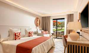 Et lyst og elegant hotelværelse med en stor seng, dekorerede puder og et privat udendørs siddeområde med udsigt over en have. (AI-genereret tekst)