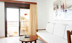 Interiør af et værelse med en sofa, et bord og et maleri af sejlbåde på væggen. Glasdør fører til en balkon. (AI-genereret tekst)