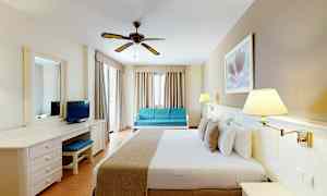 Et hotelværelse med en dobbeltseng, skrivebord, sofa og loftvifte. (AI-genereret tekst)