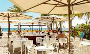 Udendørs restaurant med hvide borde og stole under parasoller, udsigt til havet. (AI-genereret tekst)