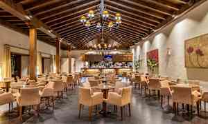 En restaurant med et højt træbjælkeloft, mange borde og stole. Væggene er dekoreret med kunstværker. (AI-genereret tekst)