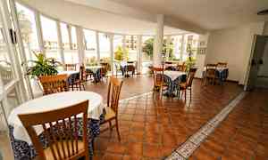 En spisestue med flere borde og stole, omgivet af vinduer med udsigt til en have. (AI-genereret tekst)