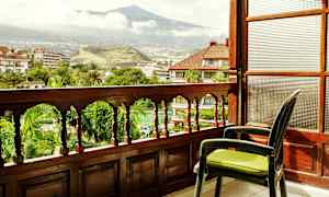 Udsigt fra en altan med trærækværk, der vender ud mod en grøn have og et bjerg i baggrunden. (AI-genereret tekst)