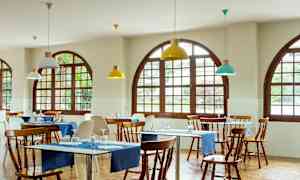 Restaurant med træborde og stole, blå bordduge og vinduer med buede rammer. (AI-genereret tekst)
