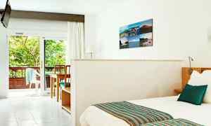 Lyst hotelværelse med seng, bord og stole samt udsigt til en frodig balkon. (AI-genereret tekst)