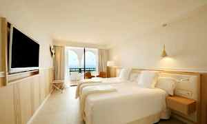 Et hotelværelse med to senge, en vægmonteret tv og en balkon med udsigt over havet. (AI-genereret tekst)