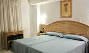 Hotelværelse med to enkeltsenge med blåt sengetøj. Træmøbler og et billede pryder væggen. (AI-genereret tekst)