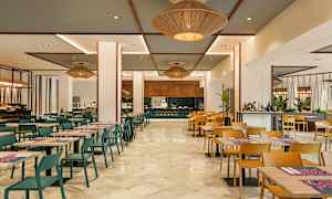 En spisesal med borde og stole, hvor en kok vises arbejde ved en madstation. (AI-genereret tekst)