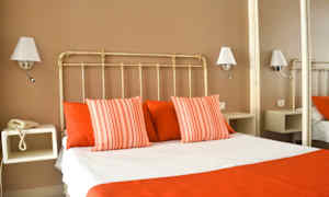 Et hotelværelse med en seng klædt i hvide og røde sengelagner, omgivet af væglamper. (AI-genereret tekst)