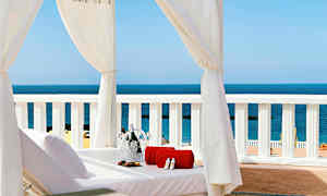 Solstol under hvid baldakin med udsigt over havet, med håndklæde og champagnekøler. (AI-genereret tekst)