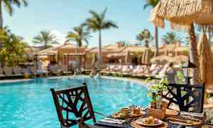 Morgenmad serveret ved et bord ved en pool med liggestole og parasoller i baggrunden. (AI-genereret tekst)