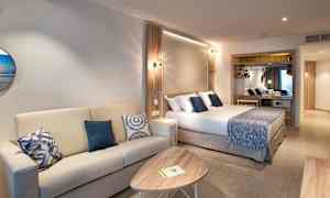 Et hotelværelse med en sofa, et sofabord og en seng med blå dekorative puder. (AI-genereret tekst)