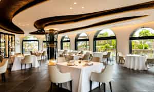 Restaurant med lyst interiør, store vinduer og dækkede borde. (AI-genereret tekst)