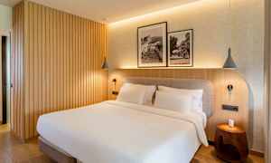 Et soveværelse med en dobbeltseng, træpanelvæg og to indrammede sort-hvide fotografier over sengen. (AI-genereret tekst)