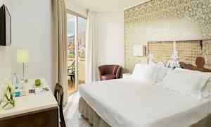 Et hotelværelse med dobbeltseng, et skrivebord med lampe og en balkon med udsigt. (AI-genereret tekst)