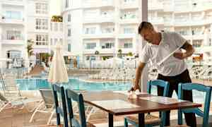 Person, der rengør et bord ved en restaurant tæt på en swimmingpool. (AI-genereret tekst)