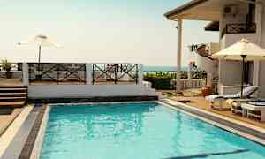 Udendørs pool ved et feriekompleks med liggestole og parasoller samt udsigt over havet. (AI-genereret tekst)