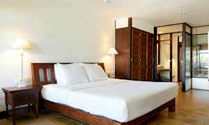 Billede af et hotelværelse med en stor seng med hvidt sengetøj, to natborde, bordlamper og skabe i træ. (AI-genereret tekst)