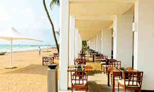 En udendørs terrasse med spiseborde og stole ved siden af en sandstrand. (AI-genereret tekst)