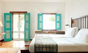 Et lyst soveværelse med en stor seng, hvide lagner og turkise skodder, der lukker naturligt lys ind. (AI-genereret tekst)