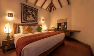 Et værelse med en stor seng, pyntet med farverige puder og et rødt tæppe. Der er en oplyst lampe på natbordet, og et dekorativt kunstværk hænger over sengen. (AI-genereret tekst)