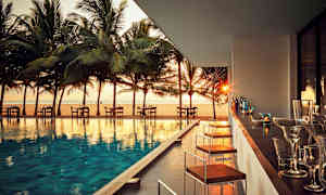 En udendørs servering ved en pool med udsigt over stranden og palmer ved solnedgang. (AI-genereret tekst)