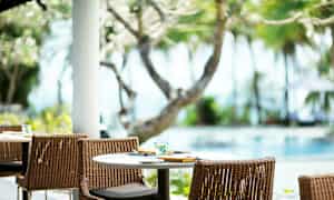 Et dækket bord med stole udendørs ved en pool, omgivet af træer og beplantning. (AI-genereret tekst)