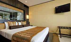 Et hotelværelse med en dobbeltseng dekoreret med brune og gyldne pyntedetaljer. Et TV hænger på væggen til højre. (AI-genereret tekst)