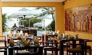 En restaurant med dækkede borde og udsigt gennem vinduer til et udemiljø med parasoller og vegetation. (AI-genereret tekst)