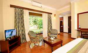 Et hotelværelse med siddepladser, bord og tv, med udsigt til en grøn have. (AI-genereret tekst)