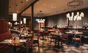 En elegant restaurant med dækkede borde og stole på et ternet gulv. Belysning hænger fra loftet. (AI-genereret tekst)