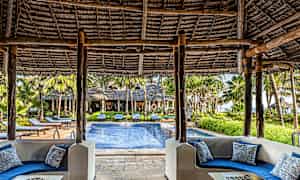 Udsigt fra et overdækket siddeområde med blå sofaer mod en pool og omliggende grønne områder. (AI-genereret tekst)