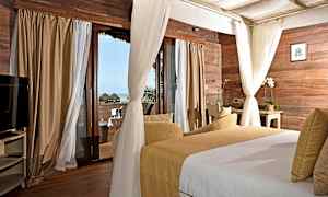 Et soveværelse med træpaneler på væggene, store vinduer med gardiner og udsigt mod havet. Værelset har en seng og en siddegruppe. (AI-genereret tekst)