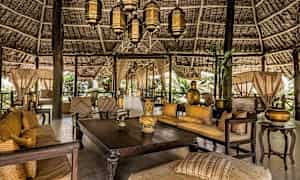 Et møbleret og dekoreret åbent område med træborde, sofaer og lanterner under et smukt stråtag. (AI-genereret tekst)