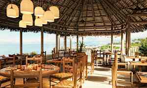 Et åbent strandnært restaurantområde med træborde og stole samt stråtag. (AI-genereret tekst)