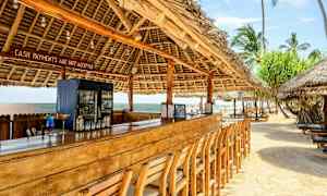 Strandbar med træbord og stole under tag af palmeblade. (AI-genereret tekst)