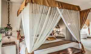 Soveværelse med en himmelseng omgivet af hvide gardiner og dekoreret med varme tonede tekstiler. (AI-genereret tekst)