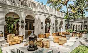 En udendørs terrasse med buer, palmer og siddepladser inspireret af arabisk design. (AI-genereret tekst)