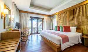 Et hotelværelse med en dobbeltseng, puder i forskellige farver, et træbord med stol og en balkon med udsigt. (AI-genereret tekst)