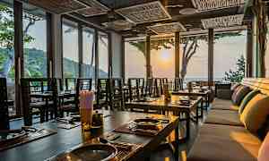 Interiør af en restaurant med dækkede borde og store vinduer, der lukker solnedgangens lys ind. (AI-genereret tekst)