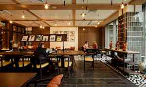 Interiør af en café eller arbejdsområde med træmøbler, dekorationer på bordet og personer, der arbejder eller samtaler. (AI-genereret tekst)