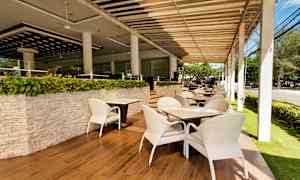 En udendørsrestaurant med hvide stole og borde på et parketgulv, omgivet af grønne planter. (AI-genereret tekst)