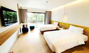 Et hotelværelse med to enkeltsenge, et fladskærms-tv på væggen og en altan med udsigt over grønne områder. (AI-genereret tekst)