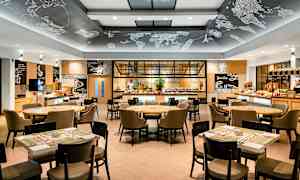 En moderne restaurantindretning med borde og stole samt en serveringsbuffet i baggrunden. (AI-genereret tekst)