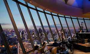 Folk sidder i en luksuriøs lounge med panoramaudsigt over byens skyline ved skumring. (AI-genereret tekst)